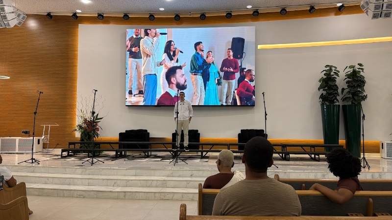 Integrante se apresentando com telão ao fundo mostrando o grupo